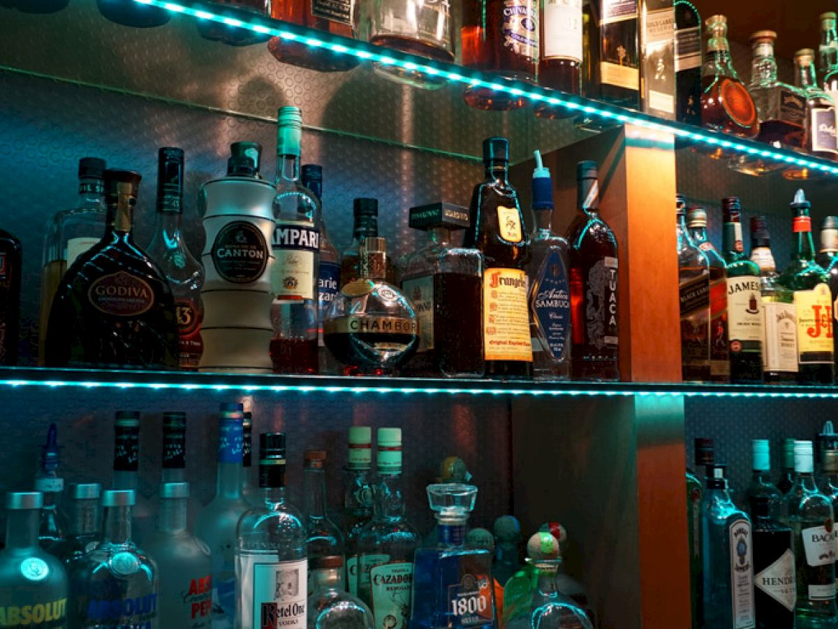 A variety of liquor bottles are displayed on illuminated shelves in a bar or lounge setting.