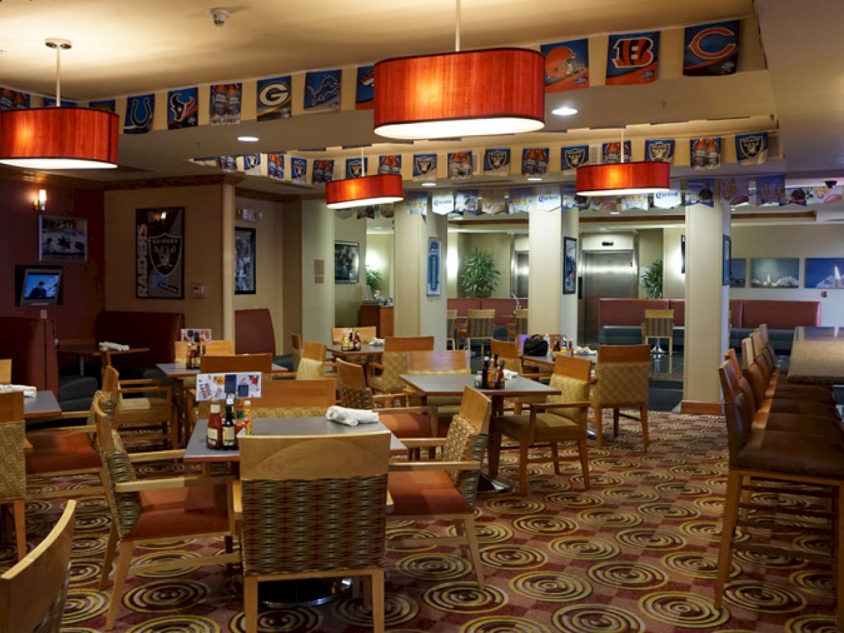 The image shows an empty restaurant with tables and chairs, sports team flags hanging from the ceiling, and a bar area on the right.