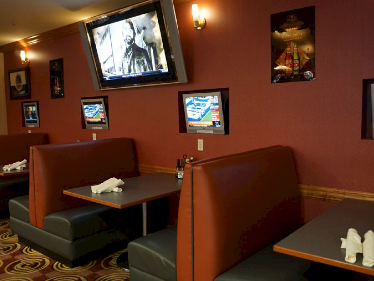 The image shows a restaurant or sports bar with booths, each equipped with individual TVs, and a larger TV on the wall. Tables are set with napkins and condiments.