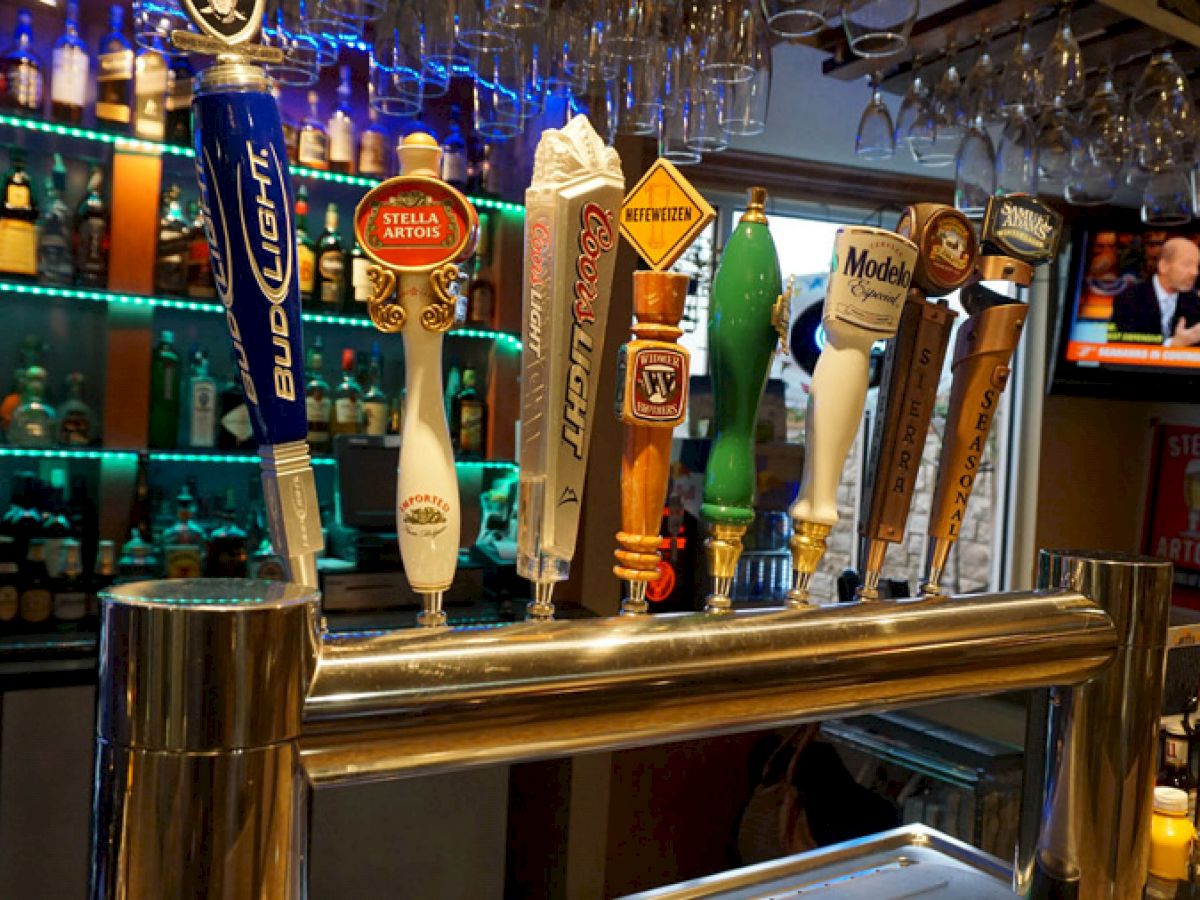 A bar setup with various beer taps, glasses, and bottles in the background, with a TV in view on the right side.