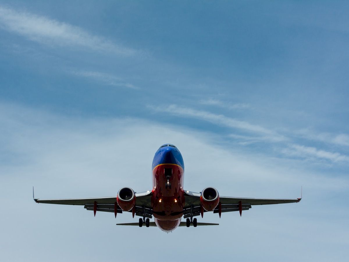 The image shows a commercial airplane flying with a clear blue sky in the background, viewed from below.