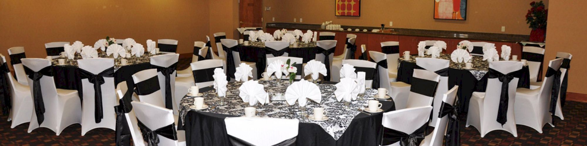 A banquet hall with round tables covered in black and white linens, elegantly decorated with folded napkins and surrounded by white chairs.