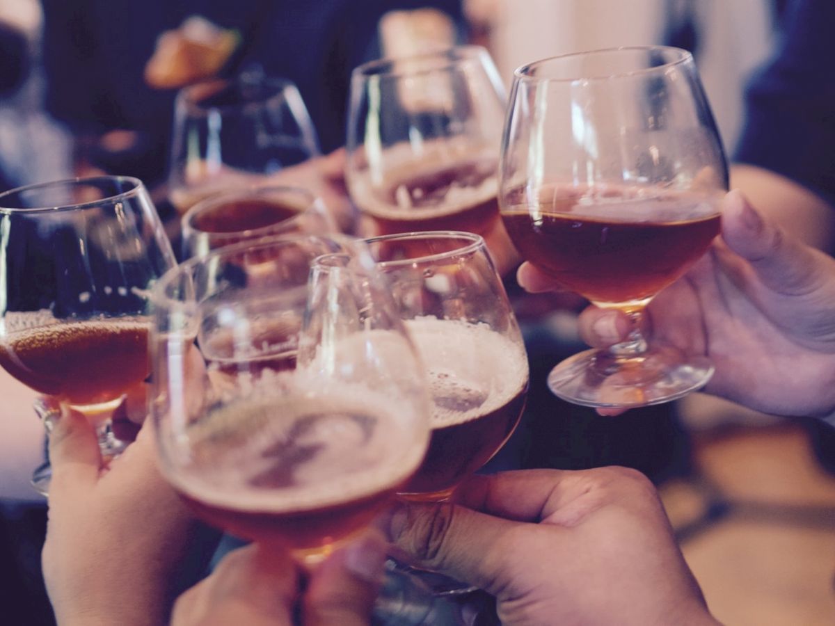 A group of hands holding glasses filled with a brownish beverage, possibly a celebratory toast during a social gathering.