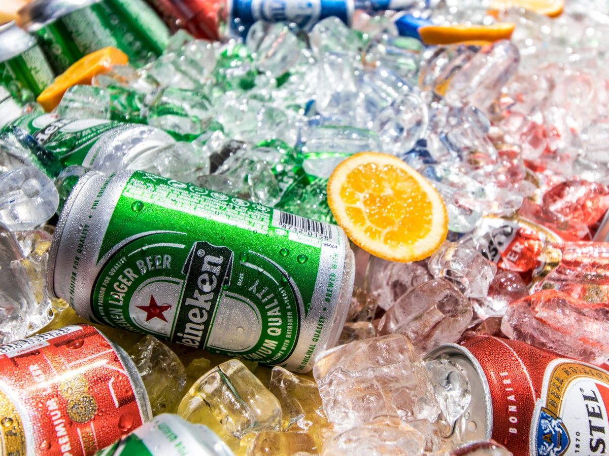 The image shows various canned beverages, including Heineken beer, chilled in ice with an orange slice among them, ideal for a refreshing treat.