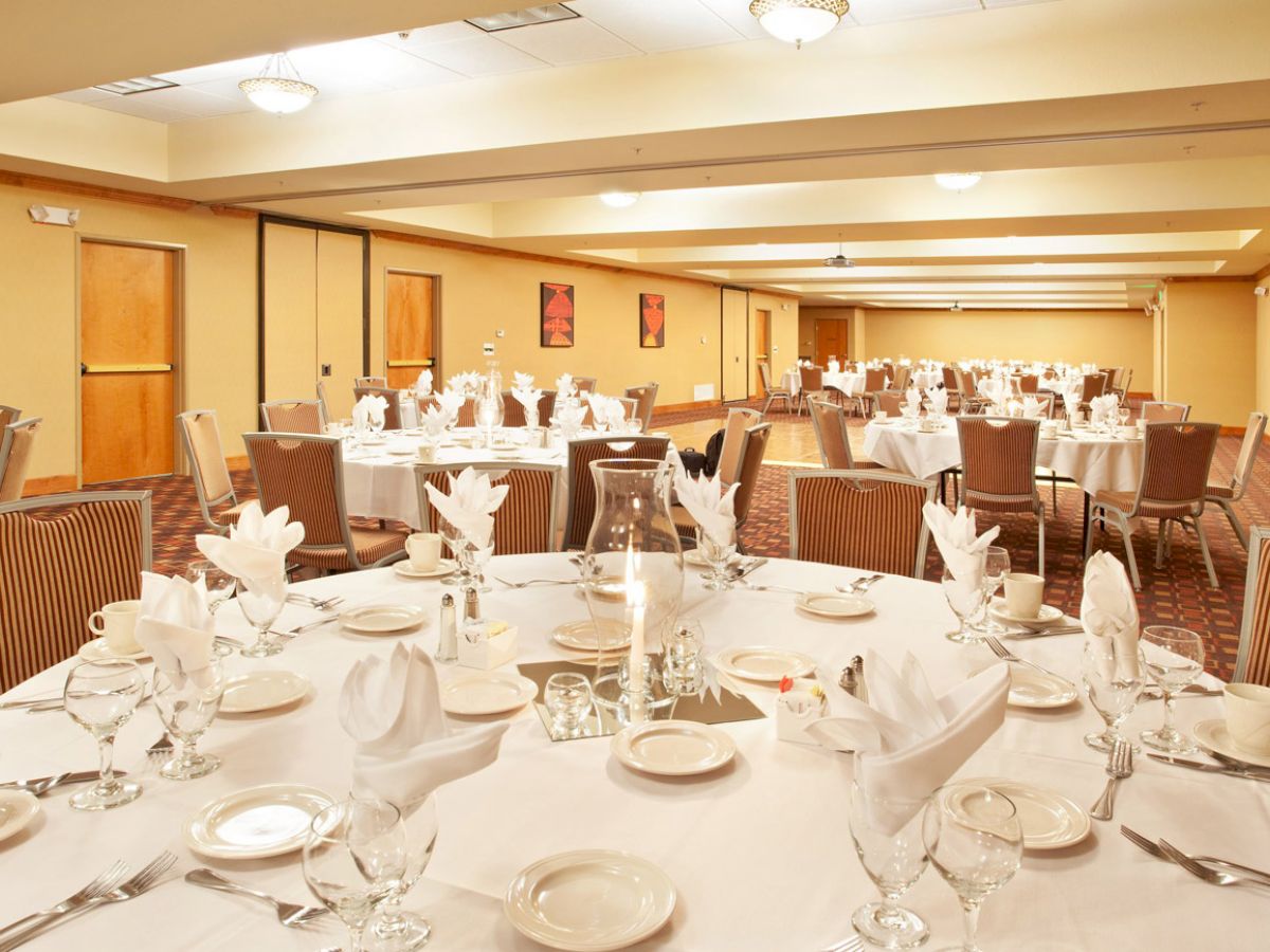 A banquet hall set up for an event with round tables adorned with white tablecloths, napkins, glassware, and cutlery.