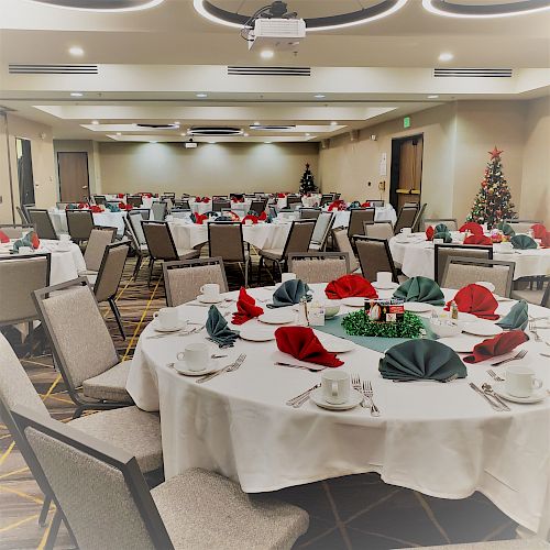 A banquet hall set with round tables, adorned with red and green napkins, festive decorations, and Christmas trees.