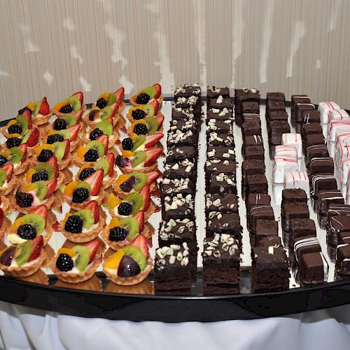 An assortment of pastries on a platter: fruit tarts on the left, chocolate brownies in the middle, and pink-striped confections on the right.