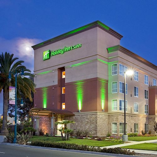 The image shows a Holiday Inn Express hotel building illuminated by green lights at dusk with palm trees and streetlights in the foreground.