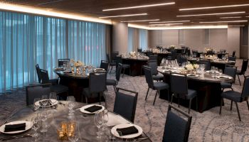 The image shows a banquet hall with round tables set for an event with glassware, plates, napkins, and centerpiece decorations.