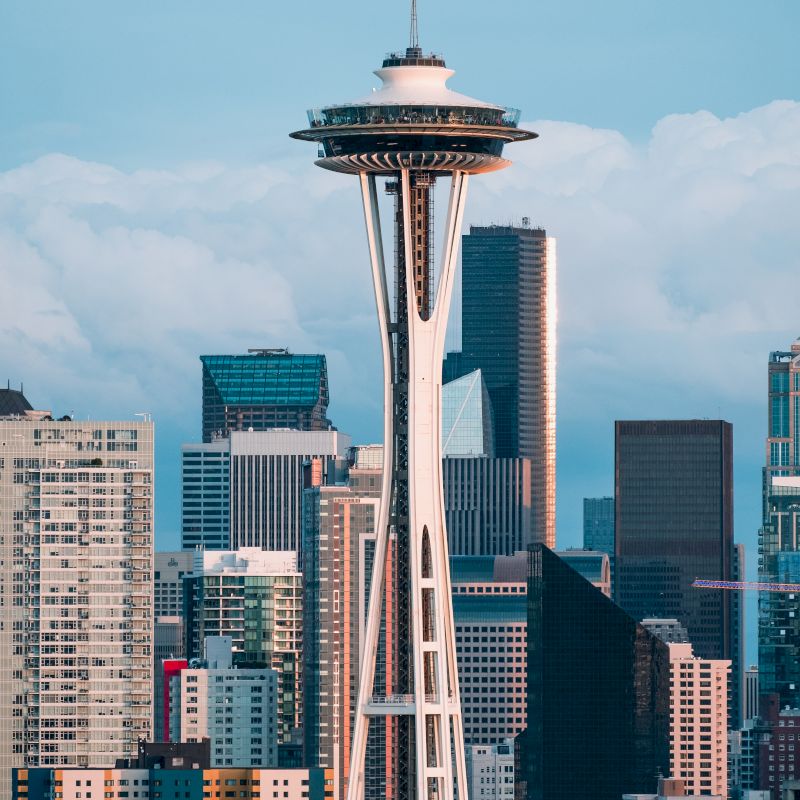 The image showcases a cityscape dominated by a tall structure resembling the Space Needle, with various high-rise buildings in the background.