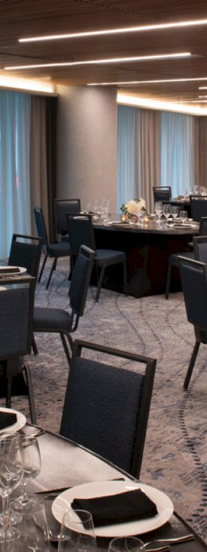 The image shows an elegantly set dining area with round tables and chairs, decorated with candles and flowers, set for an event or gathering.