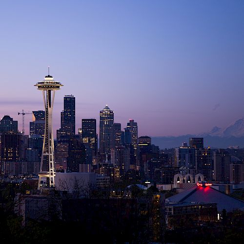 The image shows the Seattle skyline at dusk, featuring the Space Needle with Mount Rainier visible in the background.