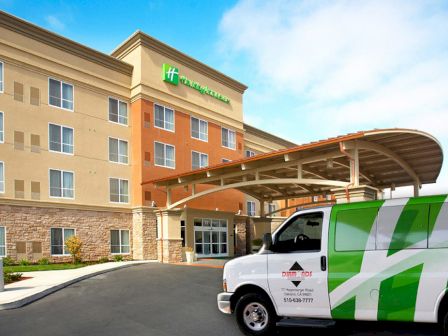 This image features the entrance of a Holiday Inn hotel building with a green and white hotel shuttle van parked in front of it.